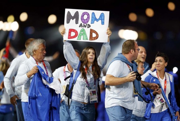 Un joven atleta de la delegación griega con un cartel que saluda a sus padres. Foto: Reuters